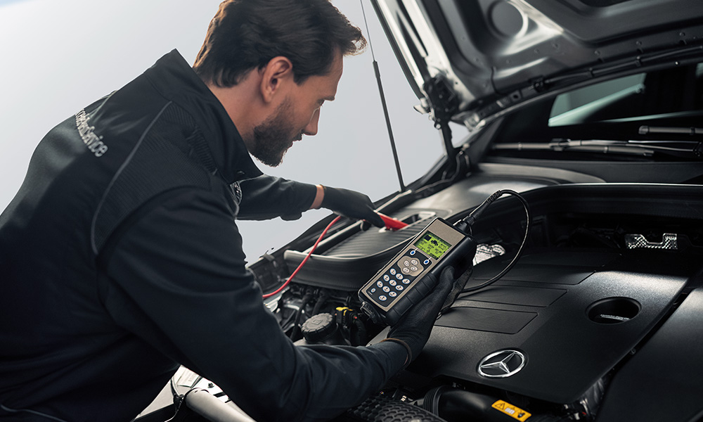 Werkstattmitarbeiter prüft die Batterie des Fahrzeugs bei geöffneter Motorhaube