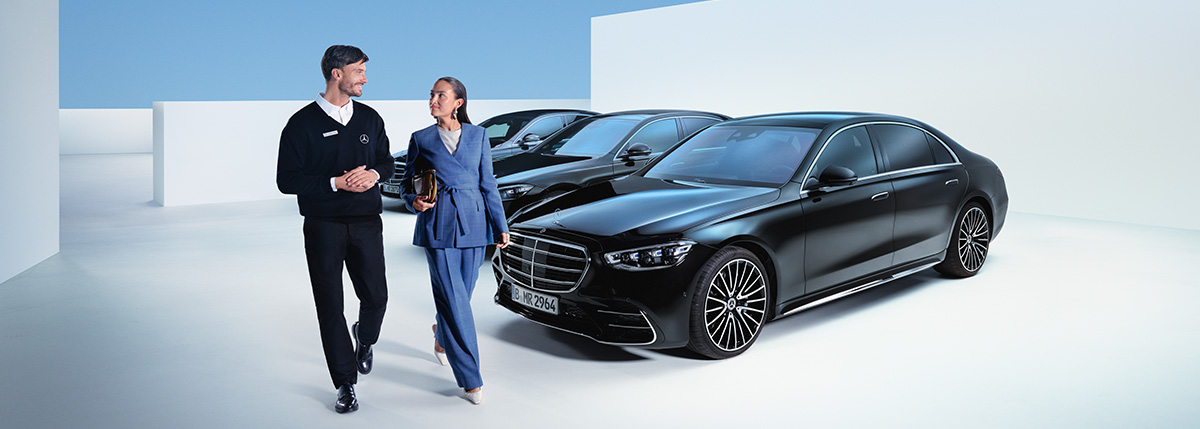Kundin im Gespräch mit Serviceberater, im Hintergrund drei dunkle Mercedes-Benz