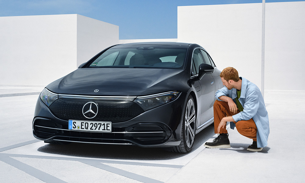 Mann kniet neben seinem schwarzen Mercedes und begutachtet den Reifen